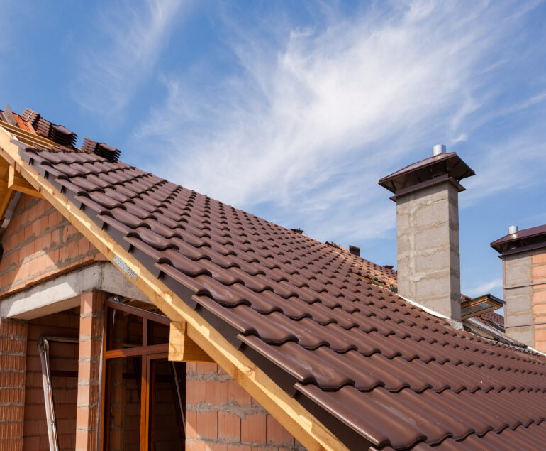 Una casa in costruzione, che vanta un tetto incompleto con tegole di metallo marrone e due camini, mette in mostra muri in mattoni a vista contro un cielo azzurro. Sotto tutto questo si nasconde la promessa di un comfort efficiente, grazie all'uso strategico di isolamento EPS per la protezione termica.